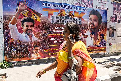 A woman walks past a banner of actor and Tamilaga Vettri Kazhagam (TVK) President Chandrasekaran Joseph Vijay, after his party surprisingly emerged as the single largest party in the April 23 polls to the Tamil Nadu state Assembly, in Chennai.