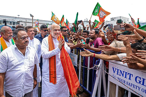 In this image posted on May 8, 2026, Union Home Minister Amit Shah greets supporters upon his arrival at the airport ahead of the BJP legislature party meeting, in Kolkata. BJP leader Suvendu Akhikari and party state president Samik Bhattacharya are also seen.