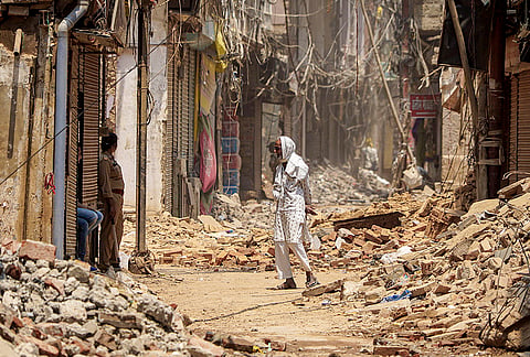 A police personnel keeps vigil as a man walks past the debris during a demolition drive at Dal Mandi area, in Varanasi, Uttar Pradesh.