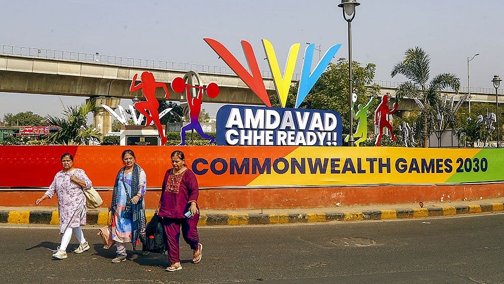 Commuters walk past newly-setup standees after the city was formally awarded hosting rights of the Commonwealth Games 2030, in Ahmedabad. - PTI