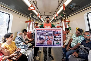 | Photo: PTI : Digital creator Arun Haryani holds a poster in a metro train, depicting use of public transport, to aware people about fuel conservation in view of Prime Minister Narendra Modi's appeal for austerity, in Ahmedabad, Gujarat.