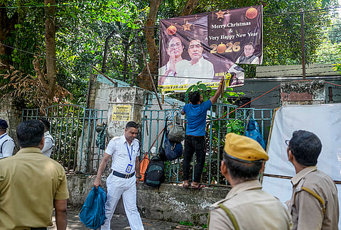 Police personnel stand guard as a municipal worker removes a hoarding featuring former West Bengal CM Mamata Banerjee and her associates from a city street, in Kolkata, West Bengal.