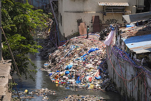 A child stands atop a heap of waste near a drain at Bandra area, in Mumbai.