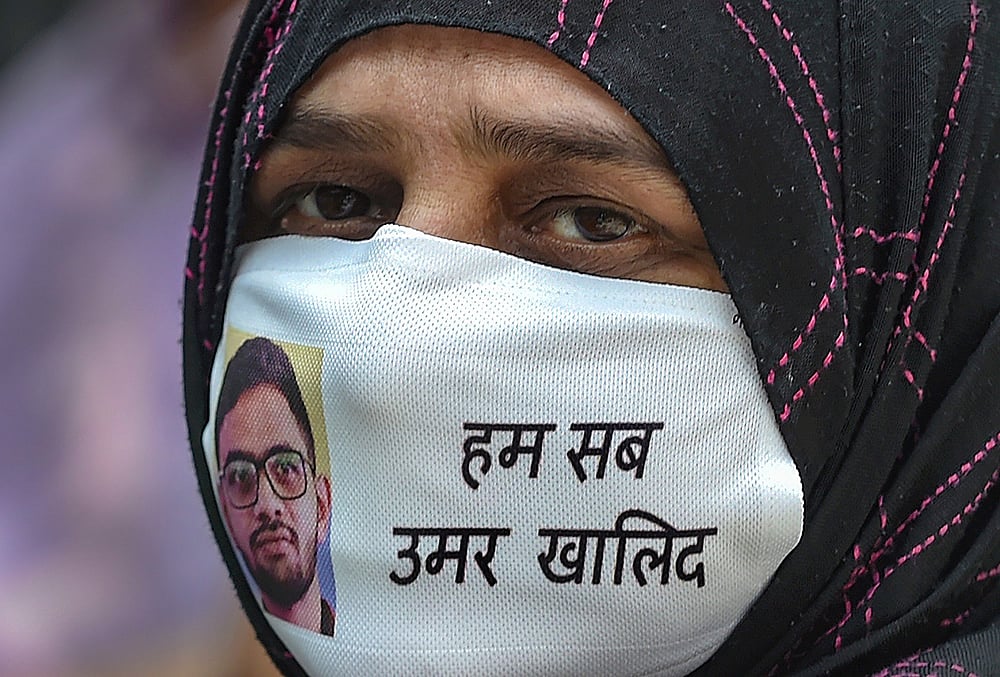 The Delhi High Court on Friday, May 22, 2026, granted three-day interim bail to activist Umar Khalid, who is in custody in a case under anti-terror law UAPA concerning the "larger conspiracy" behind the February 2020 riots in the city's northeastern parts, to enable him to meet his mother who has to undergo a surgery. Sabiha, mother of Umar Khalid, is seen wearing a mask bearing her son's image, during a press conference over police probe in the Delhi riots case, at the Press Club of India, in New Delhi, in this file photo dated Wednesday, Sept. 16, 2020.  - | Photo: PTI/Vijay Verma