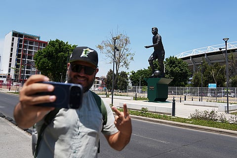 A fan takes a picture with a statue of Brazilian soccer player in the background after its unveiling outside Jalisco Stadium in Guadalajara, Mexico.