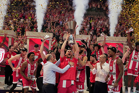 Olympiacos' Kostas Papanikolaou lifts the trophy next to Olympiacos' presidents Giorgos Aggelopoulos, left, and Panagiotis Aggelopoulos right ,after winning the Euroleague final basketball match against Real Madrid in Athens, Greece.