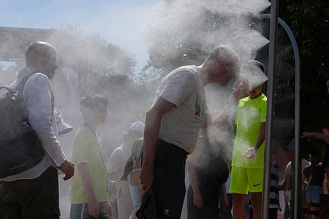 Visitors cool themselves with water from sprinklers during a hot day at the French Open tennis tournament in Paris.