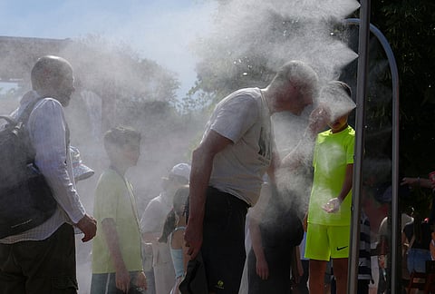 Visitors cool themselves with water from sprinklers during a hot day at the French Open tennis tournament in Paris.