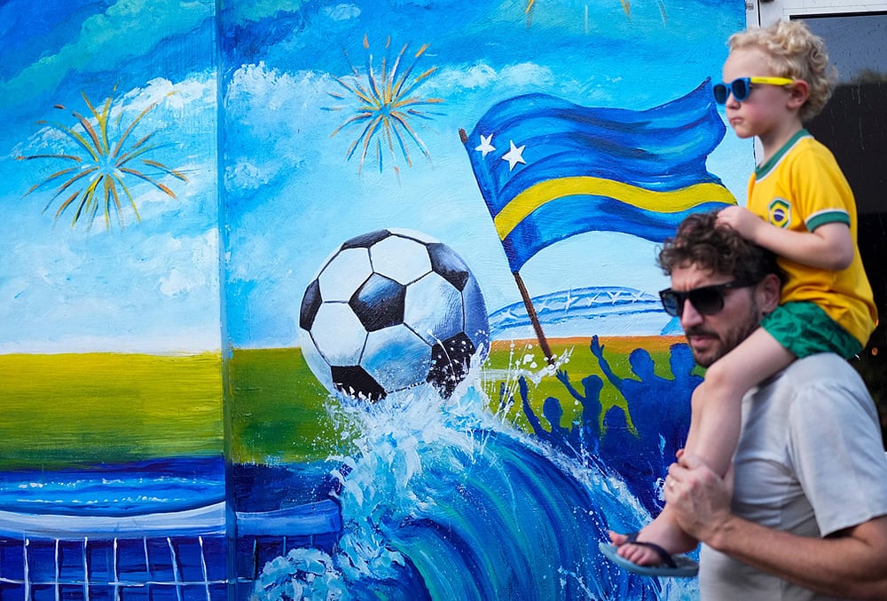Tourists walk past a mural celebrating Curacaos qualification for the FIFA World Cup in Willemstad, Curacao.