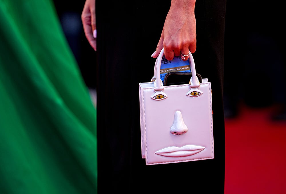 A woman holding a purse decorated with a depiction of a face poses for photographers upon arrival at the premiere of the film 'Hope' at the 79th international film festival, Cannes, southern France. - | Photo: AP/Andreea Alexandru