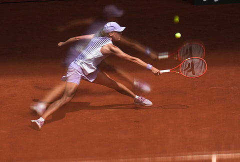 Iga Swiatek of Poland is reflected in a glass as she returns to Magda Linette of Poland during their third round women's singles tennis match at the French Open tennis tournament in Paris.