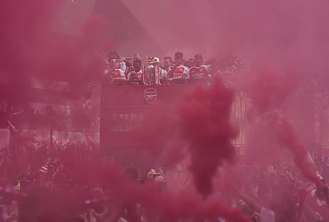 The Arsenal team on an open top bus present the trophy to fans, surrounded by red flare smoke, during a parade for winning the English Premier League title, in London.