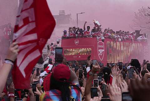 Arsenal's Bukayo Saka, right, lifts the trophy during a parade for winning the English Premier League title, in London.