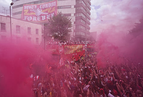 The Arsenal team on an open top bus present the trophy to fans, surrounded by red flare smoke, during a parade for winning the English Premier League title, in London.