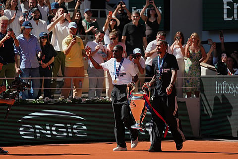 PSG's Ousmane Dembele, left, and Bradley Barcola walk onto the court with the Champions League trophy during the French Open in Paris.