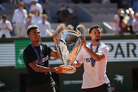 PSG's Desire Doue, left, and Warren Zaire-Emery walk onto the center court with Chgampions league trophy at the French Open tennis tournament in Paris,