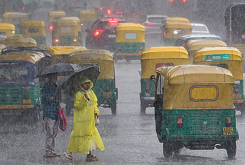 People cover themselves amid heavy rainfall, in Bengaluru, Karnataka.