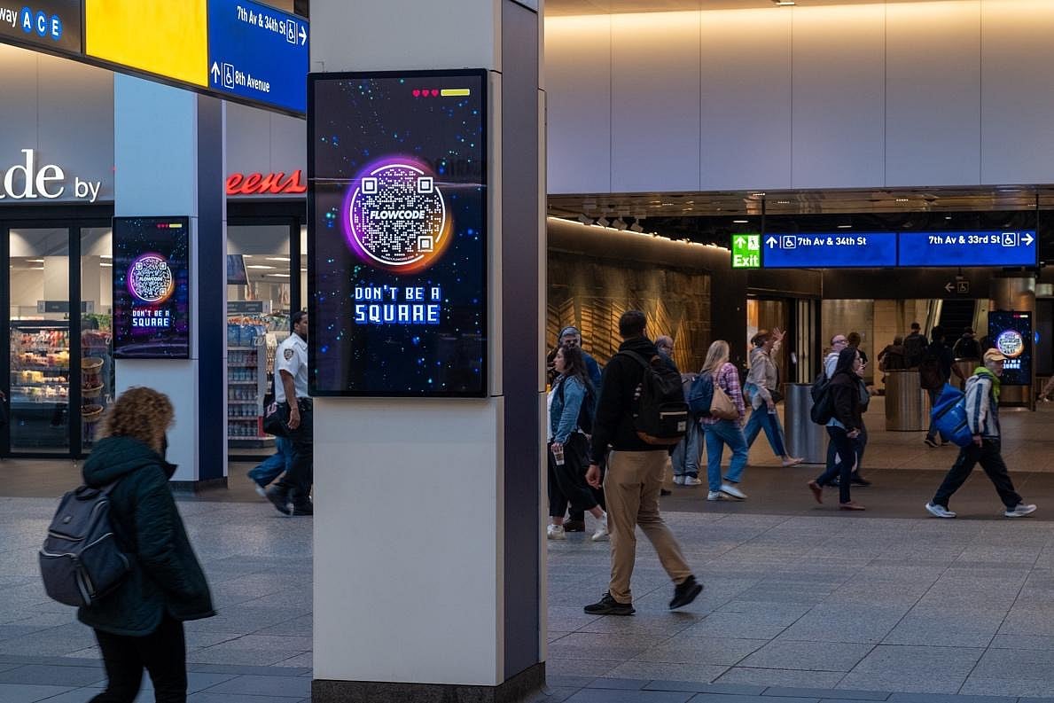 People walking through a modern transit station with a digital advertising display.