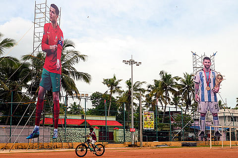 A child rides past towering cutouts of Portugal National team footballer Cristiano Ronaldo and Argentina National team footballer Lionel Messi amid the ongoing FIFA World Cup 2026, in Thiruvananthapuram, Kerala.