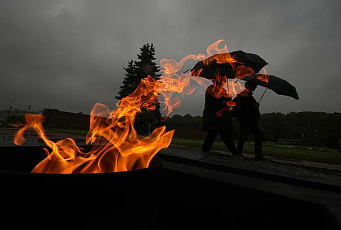 People walk past an eternal flame at the Mars Field during the rain in St. Petersburg, Russia.