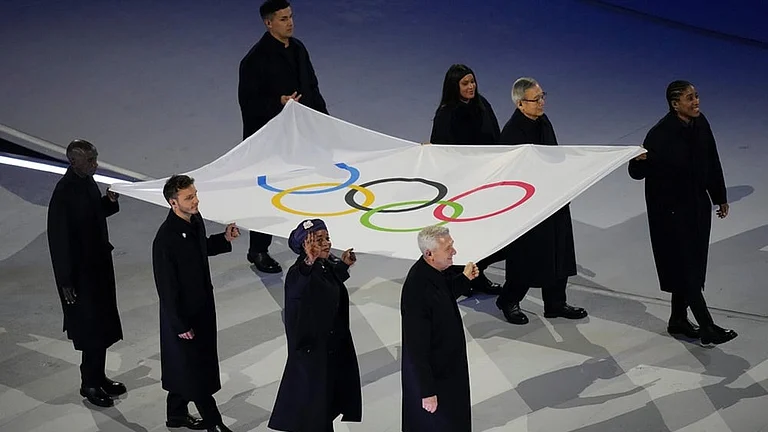 The Olympic flag is carried by Tadatoshi Akiba, second from right, Rebeca Andrade, Maryam Bukar Hassan, Nicolò Govoni, second from left, Filippo Grandi, Eliud Kipchoge, left, Cindy Ngamba, right, and Pita Taufatofua during the Olympic opening ceremony at the 2026 Winter Olympics, in Milan, Italy. - | Photo: AP/Francisco Seco