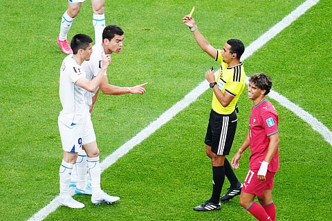 Referee Jalal Jayed, of Morocco, shows a yellow card to Uzbekistan's Odiljon Xamrobekov, left