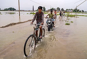 | Photo: PTI : People wade through a waterlogged road at Morisutipam village in Morigaon district, Assam.