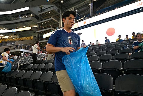 Japan fans collect trash from the stadium after the World Cup Group F soccer match between Japan and Sweden in Arlington, Texas, near Dallas.
