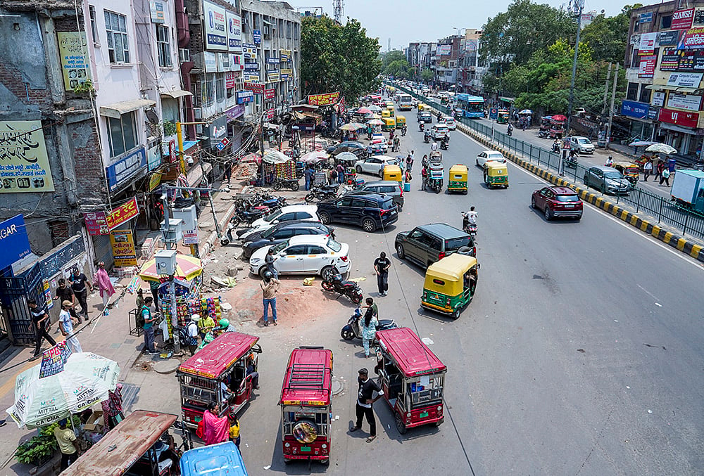 Vehicles, roadside vendors and commercial encroachments occupy a footpath, forcing pedestrians to use the carriageway, at Laxmi Nagar, in New Delhi. The Supreme Court has held that the right to walk on a demarcated footpath is a fundamental right.  - | Photo: PTI/Arun Sharma
