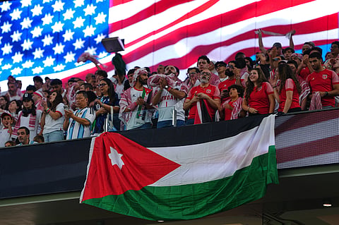 Fans hold a Jordanian flag while listening to the United States' national anthem ahead of during the World Cup Group J soccer match between Jordan and Argentina in Arlington, Texas, near Dallas, Saturday, June 27, 2026