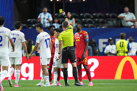 Referee Felix Zwayer, of Germany, issues a yellow card to Congo's Nathanael Mbuku (7) as Congo's Chancel Mbemba (22) smiles while Uzbekistan's Dostonbek Khamdamov (17) and Abbosbek Fayzullaev (22) pause on the pitch during the World Cup Group K soccer match between DR Congo and Uzbekistan in Atlanta, Saturday, June 27, 2026.
