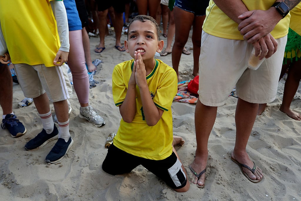 A young Brazil fan kneels before Brazil scored its second, winning goal against Japan during a live broadcast of the World Cup soccer match on Copacabana beach in Rio de Janeiro
