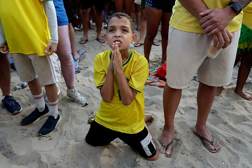 A young Brazil fan kneels before Brazil scored its second, winning goal against Japan during a live broadcast of the World Cup soccer match on Copacabana beach in Rio de Janeiro