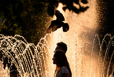 A couple walks by a public fountain on a torrid day, as the National Weather forecaster issued an extreme heat code red warning for parts of the country, in the coming days in Bucharest, Romania, Saturday, June 27, 2026. 