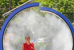 A woman cools off in a water mist machine installed by city administration to assist people in coping with the heat on a torrid day, as the National Weather forecaster issued an extreme heat code red warning for most parts of the country, in Bucharest, Romania, Monday, June 29, 2026. - | Photo: AP/Vadim Ghirda