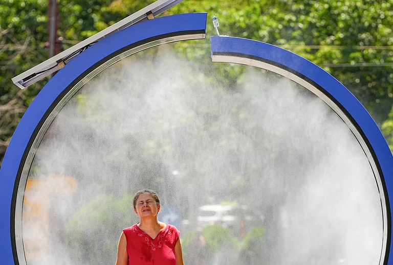 A woman cools off in a water mist machine installed by city administration to assist people in coping with the heat on a torrid day, as the National Weather forecaster issued an extreme heat code red warning for most parts of the country, in Bucharest, Romania, Monday, June 29, 2026. - | Photo: AP/Vadim Ghirda