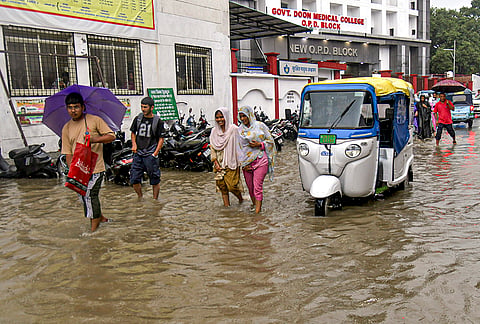 Commuters wade through a waterlogged road amid rainfall, outside Government Doon Medical College, in Dehradun, Uttarakhand.