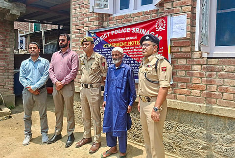 Police officials stand outside the attached residential house of slain terrorist Junaid Ahmad Bhat during legal proceedings at Thokerpora, Quimoh, in Kulgam district. The attachment was carried out by a Srinagar Police team led by SDPO Nehru Park DySP Junaid Ahmad and SHO Harwan. 