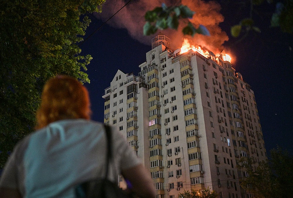 A woman looks at an apartment building burning after a Russian missile attack in Kyiv, Ukraine. - | Photo: AP/Danylo Antoniuk
