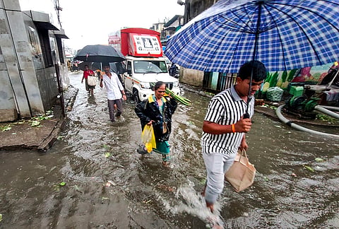 Pedestrians make their way through a waterlogged road amid rainfall, in Navi Mumbai, Maharashtra.