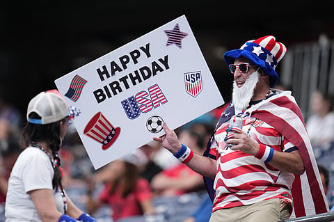 A fan wearing a U.S. flag and holding a placard reading "Happy Birthday" in celebration of America's 250th birthday waits before the World Cup round of 16 soccer match between Canada and Morocco
