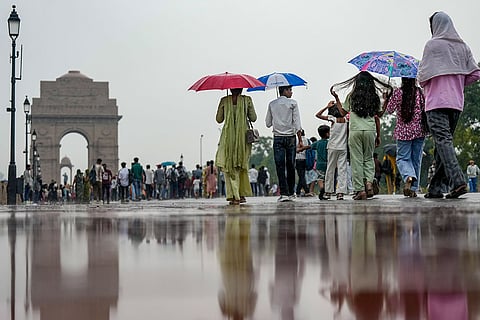 People carrying umbrellas walk near India Gate amid rain, in New Delhi.