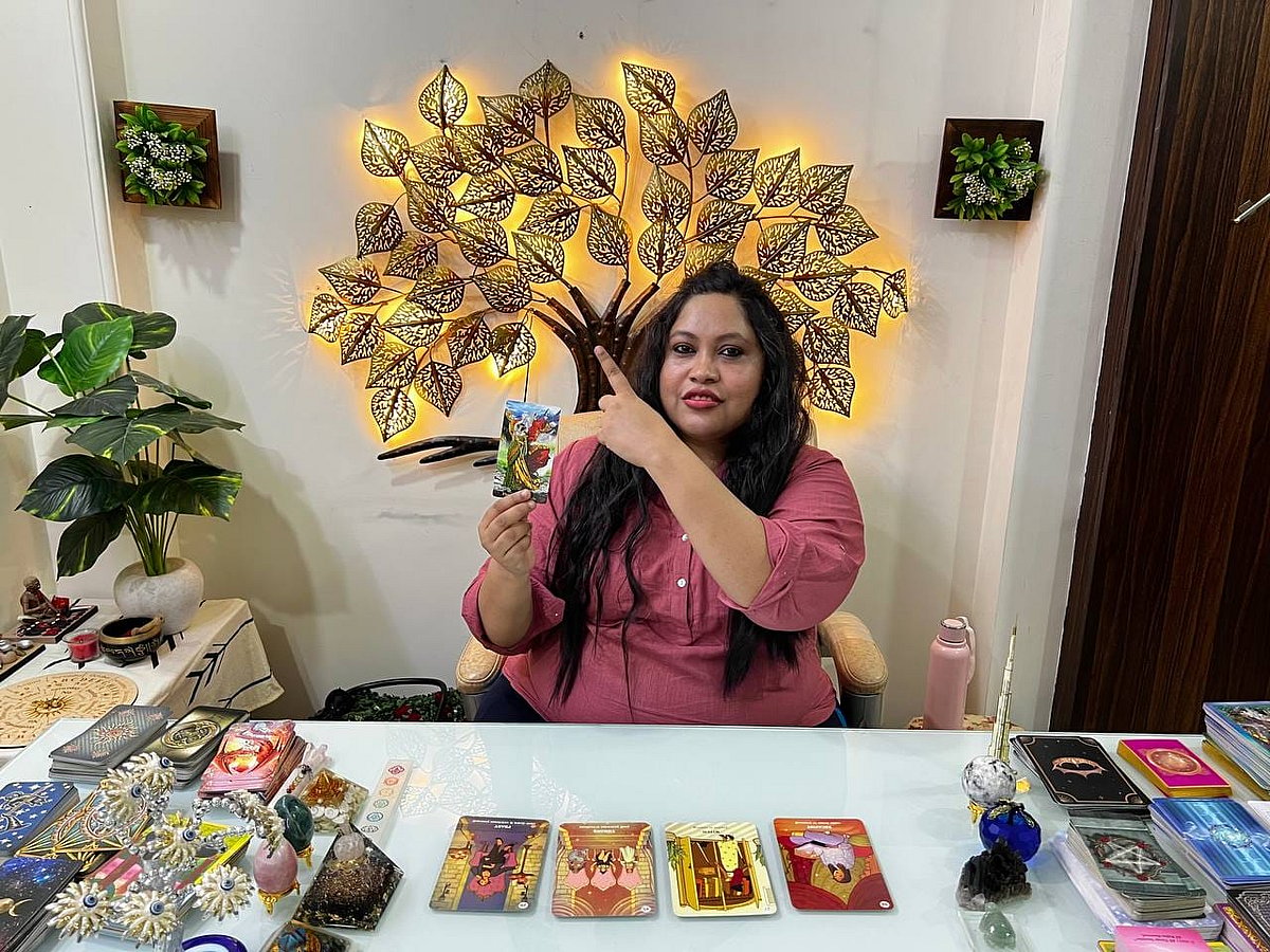 Tarot card reader Aryya Roy holding up a card under a lighted tree decor
