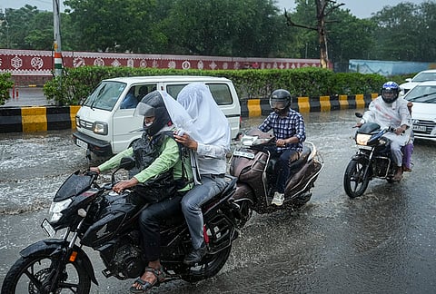 Commuters cover themselves amid rainfall, at Nizamuddin, in New Delhi, Tuesday, July 7, 2026. 
