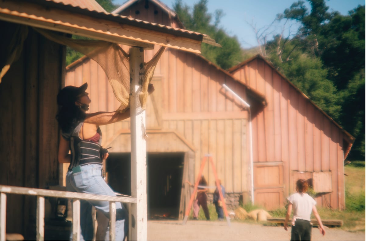 A person on a wooden porch adjusts a piece of fabric hanging near the roof