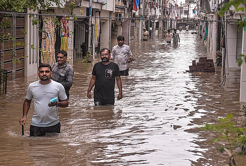 Pedestrians make their way through a severely waterlogged road following heavy rainfall, in Surat, Gujarat, Wednesday, July 8, 2026. 