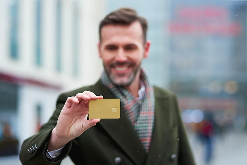 Smiling man holding up a blank gold credit card