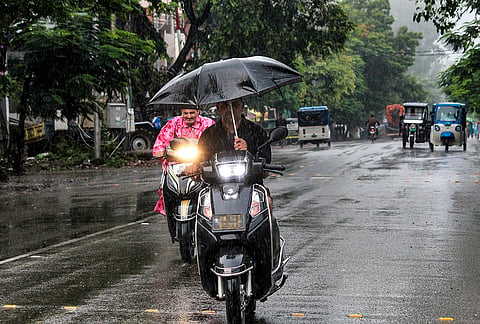 A commuter covers himself amid rainfall, in Rishikesh, Uttarakhand.