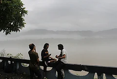People sit at a platform amid misty morning following rainfall, in Rishikesh, Uttarakhand. - | Photo: PTI