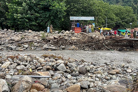 People stand near a damaged road following flash floods triggered by a cloudburst in the Overa area, near Pahalgam, Anantnag district, Jammu and Kashmir.